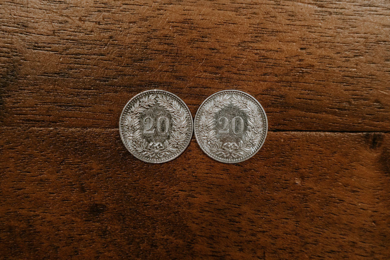two round silver-colored 20 coins on brown surface
