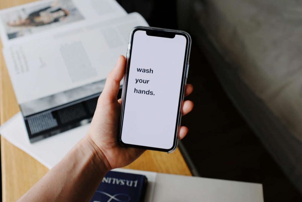 A hand holds a smartphone displaying a 'wash your hands' reminder, highlighting hygiene awareness.