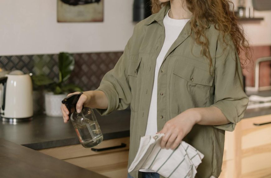 A woman with curly hair cleans a kitchen counter using a spray bottle and cloth.