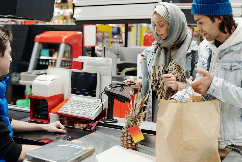 A couple in a supermarket checkout using mobile payment with a cashier. Modern retail technology.