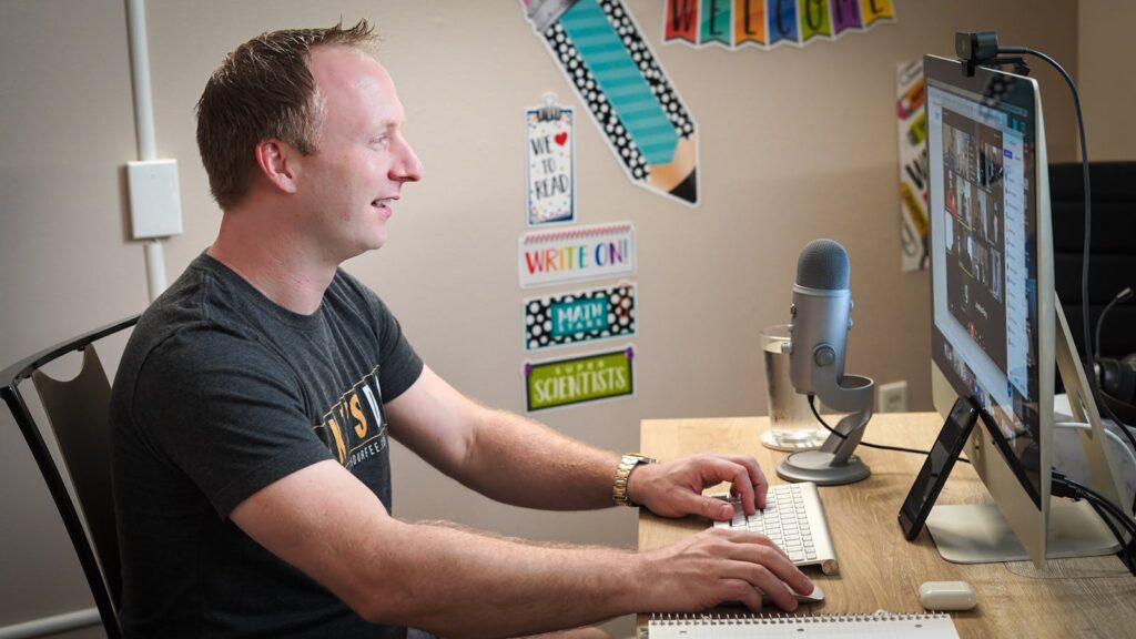 Adult man engaged in a video call on a computer in a home office setting with a microphone.
