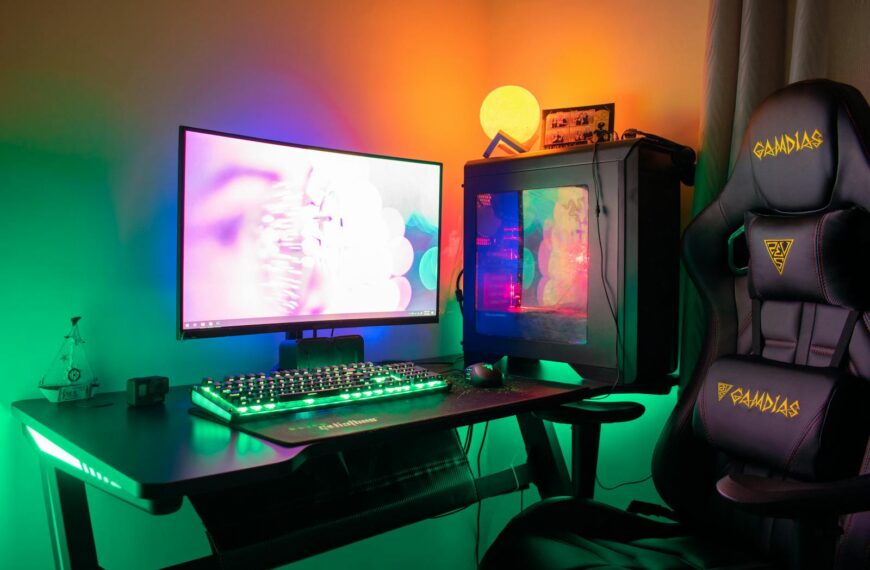 A colorful gaming setup featuring a PC, monitor, and gaming chair with RGB lights in a dark room.