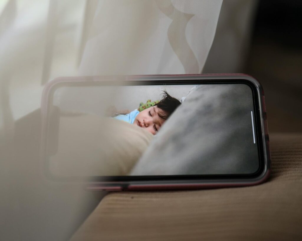 A smartphone displaying a sleeping baby in a cozy, indoor setting, conveying warmth and care.