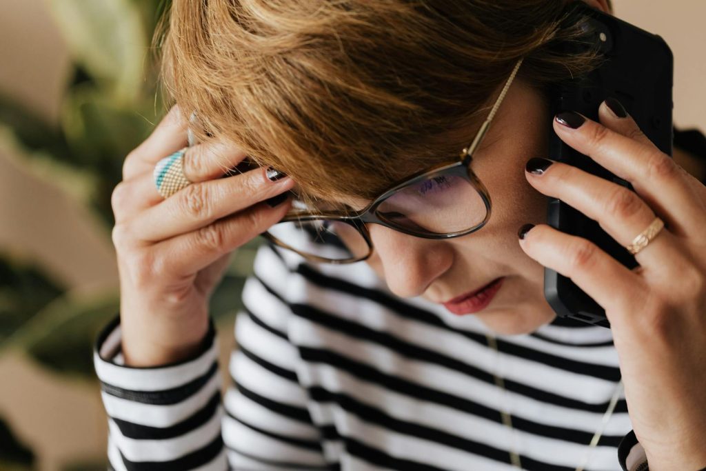 Focused woman with eyeglasses discussing work over a phone call, looking concerned and thoughtful.