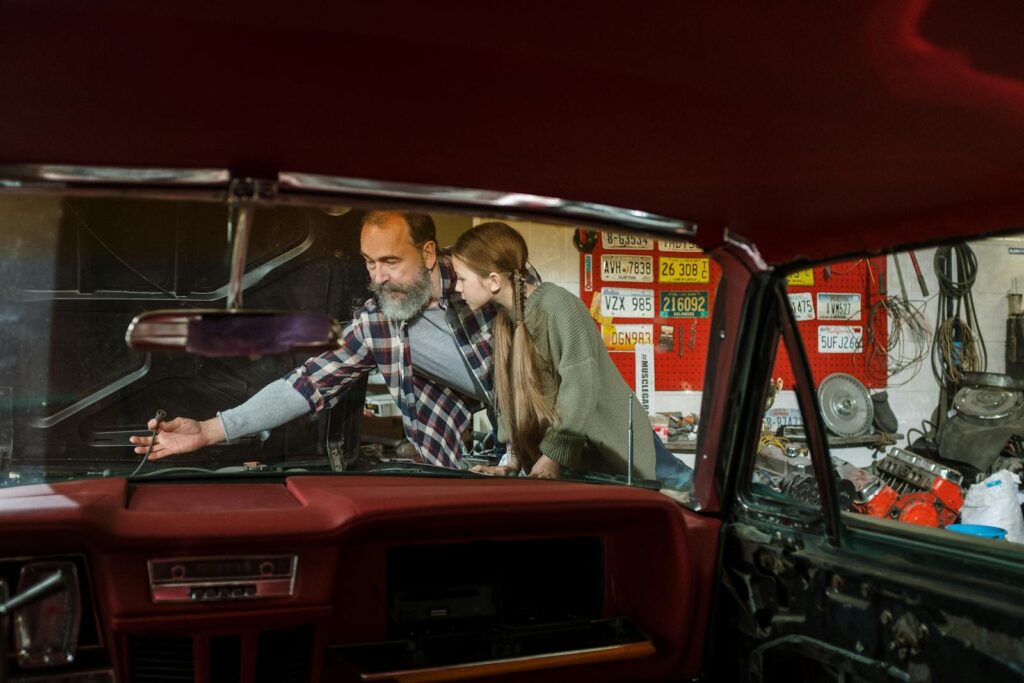 Father and daughter bonding while repairing a car together in a garage workshop. Learning and teamwork.