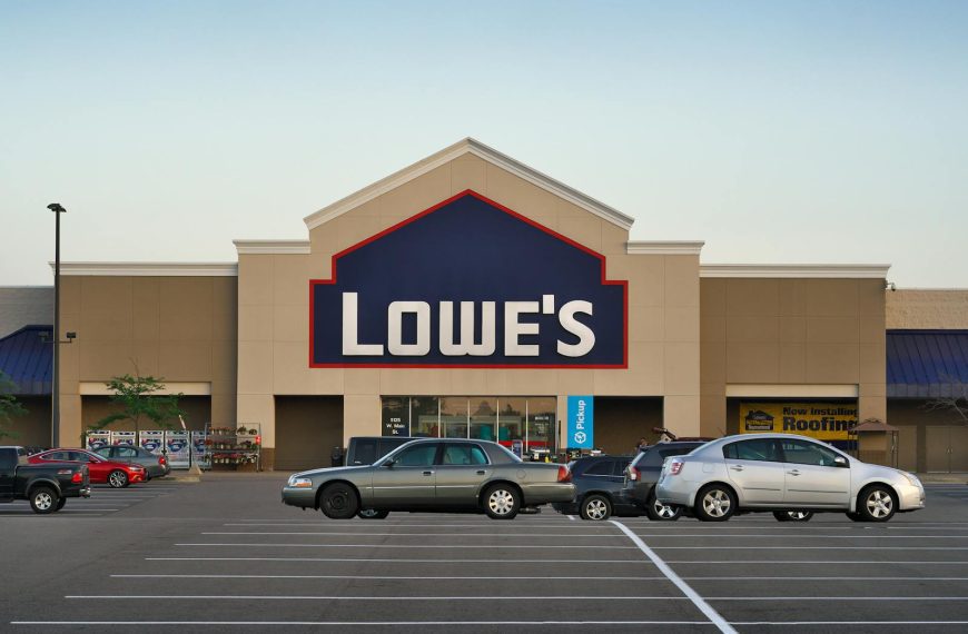 Front view of a Lowe's store entrance with parked cars in the lot during the day.