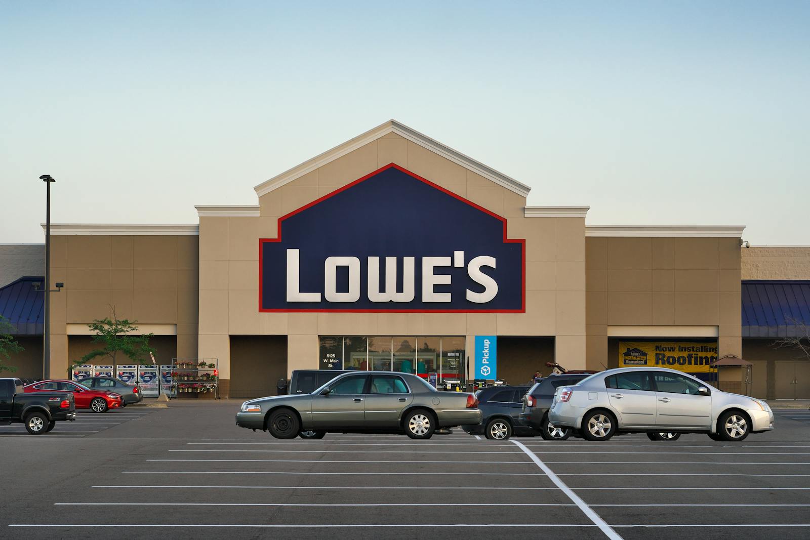 Front view of a Lowe's store entrance with parked cars in the lot during the day.