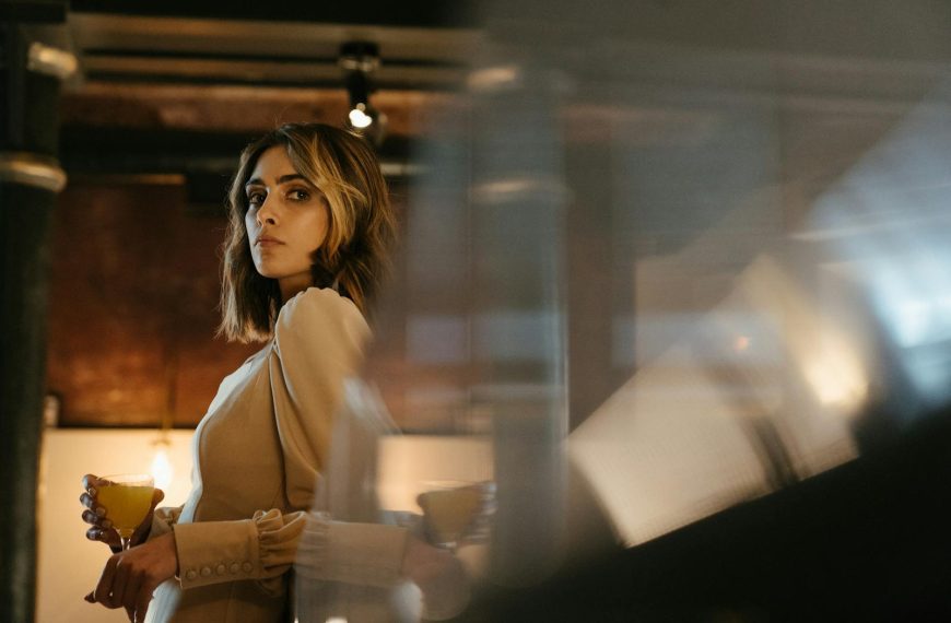 A refined woman in an elegant dress holding a drink in a stylish bar setting.