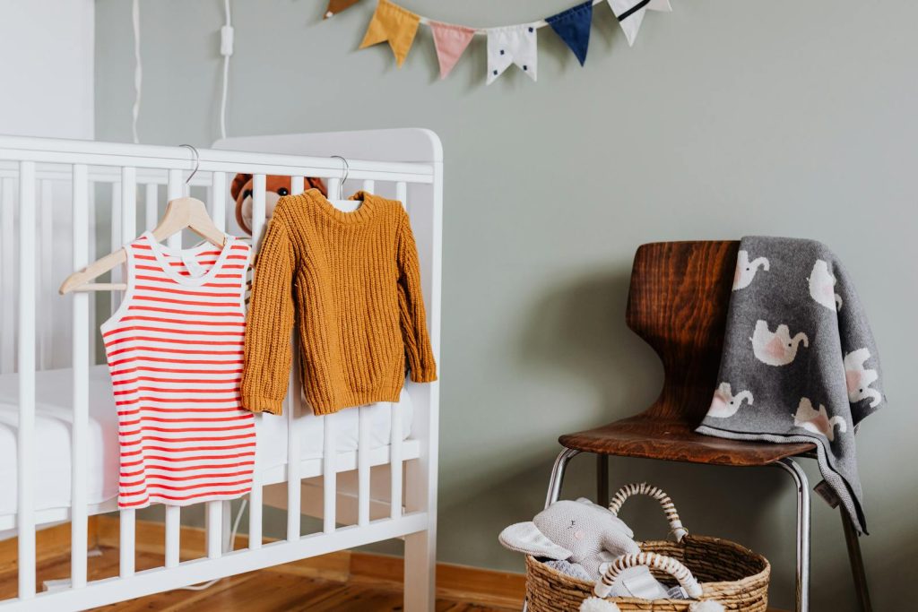 Warm and inviting nursery featuring a crib with knit sweater and striped dress on hangers.