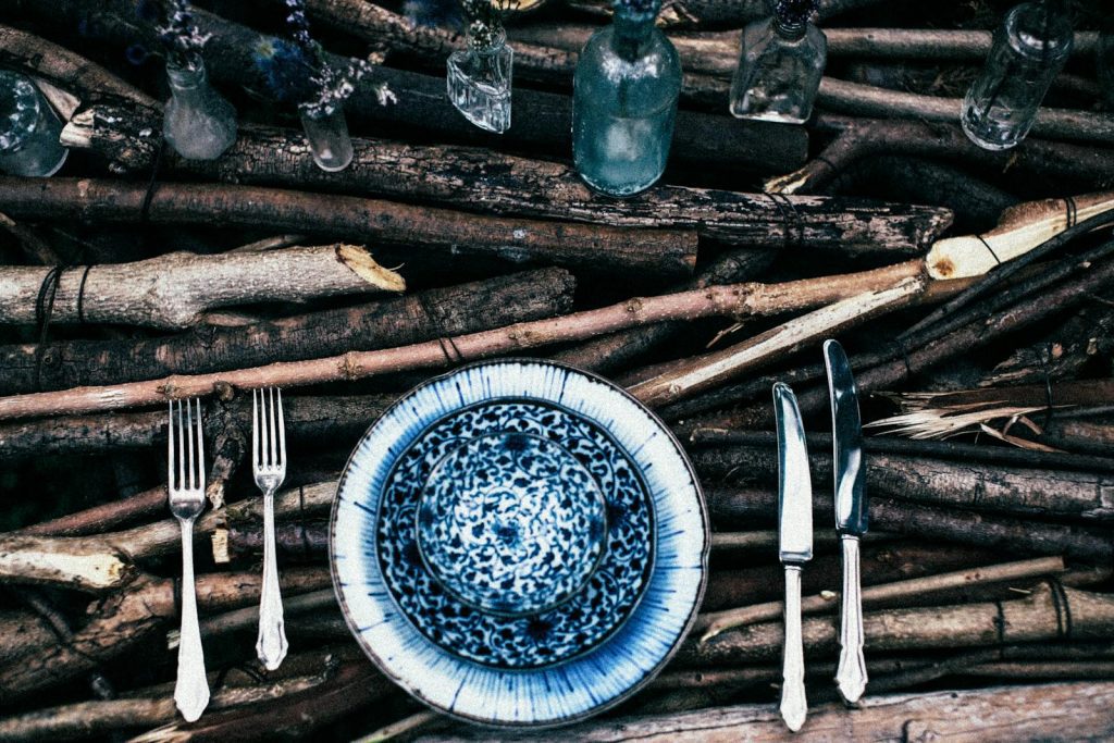 A boho-style rustic table setting outdoors featuring cutlery, plates, and glassware on wooden branches.