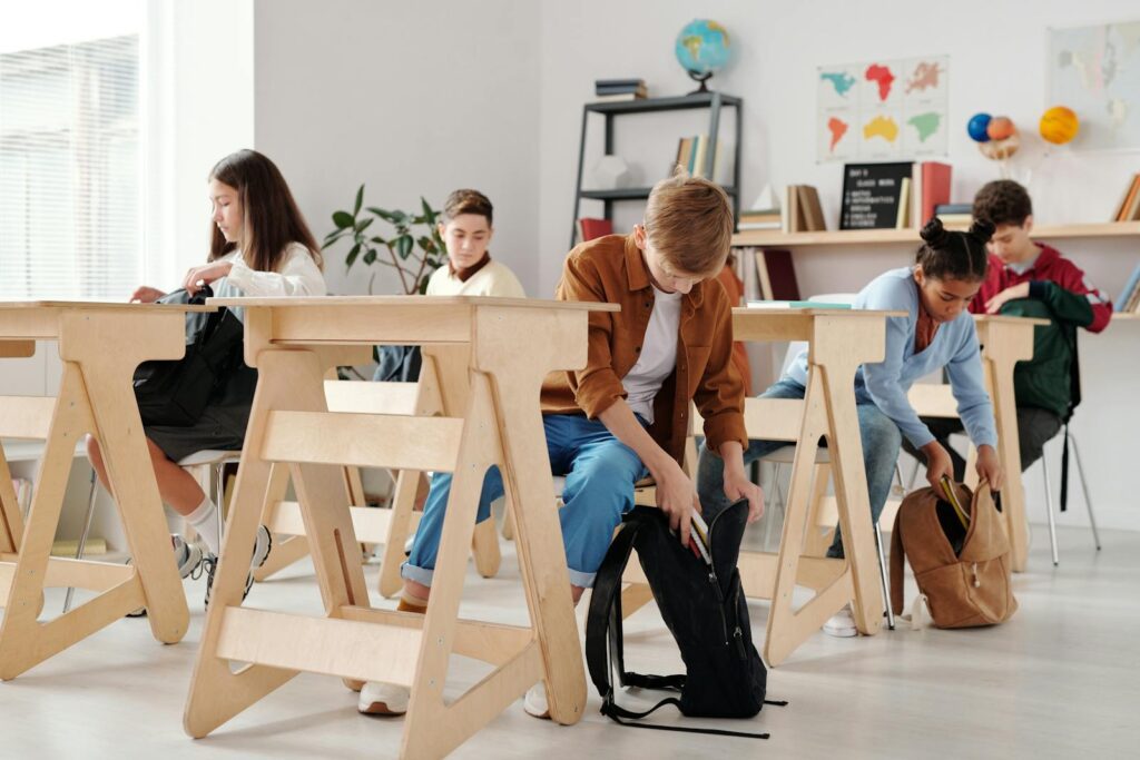 Teen students organizing backpacks in a bright classroom setting.
