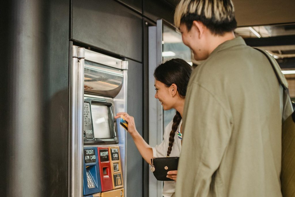 Young couple smiles while purchasing tickets at a station vending machine.