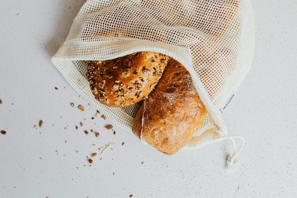 Close-up of artisan bread in a reusable mesh bag on a white surface, showcasing zero-waste lifestyle.