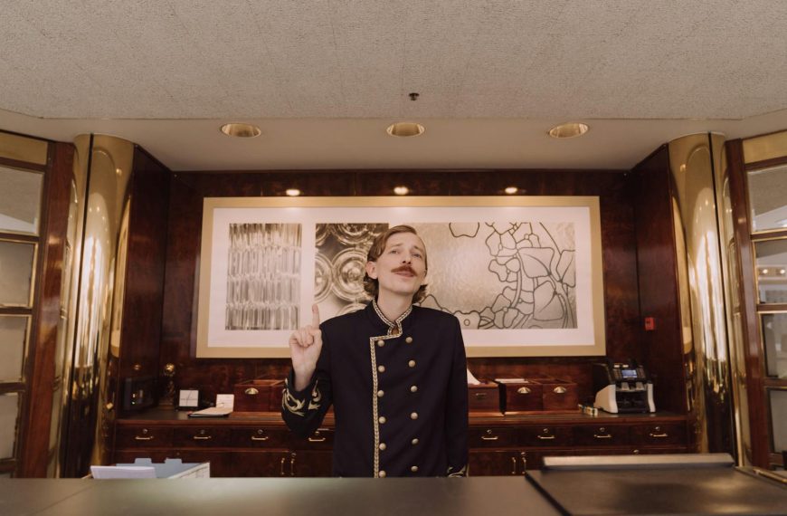 A luxury hotel receptionist in uniform stands behind the opulent front desk, ready to assist guests.