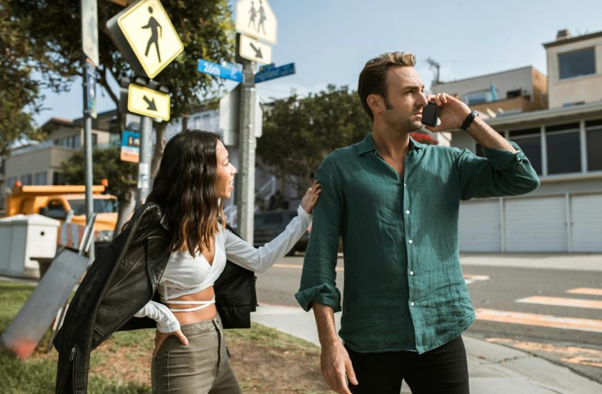 A couple has an intense discussion outdoors on a sunny street corner.