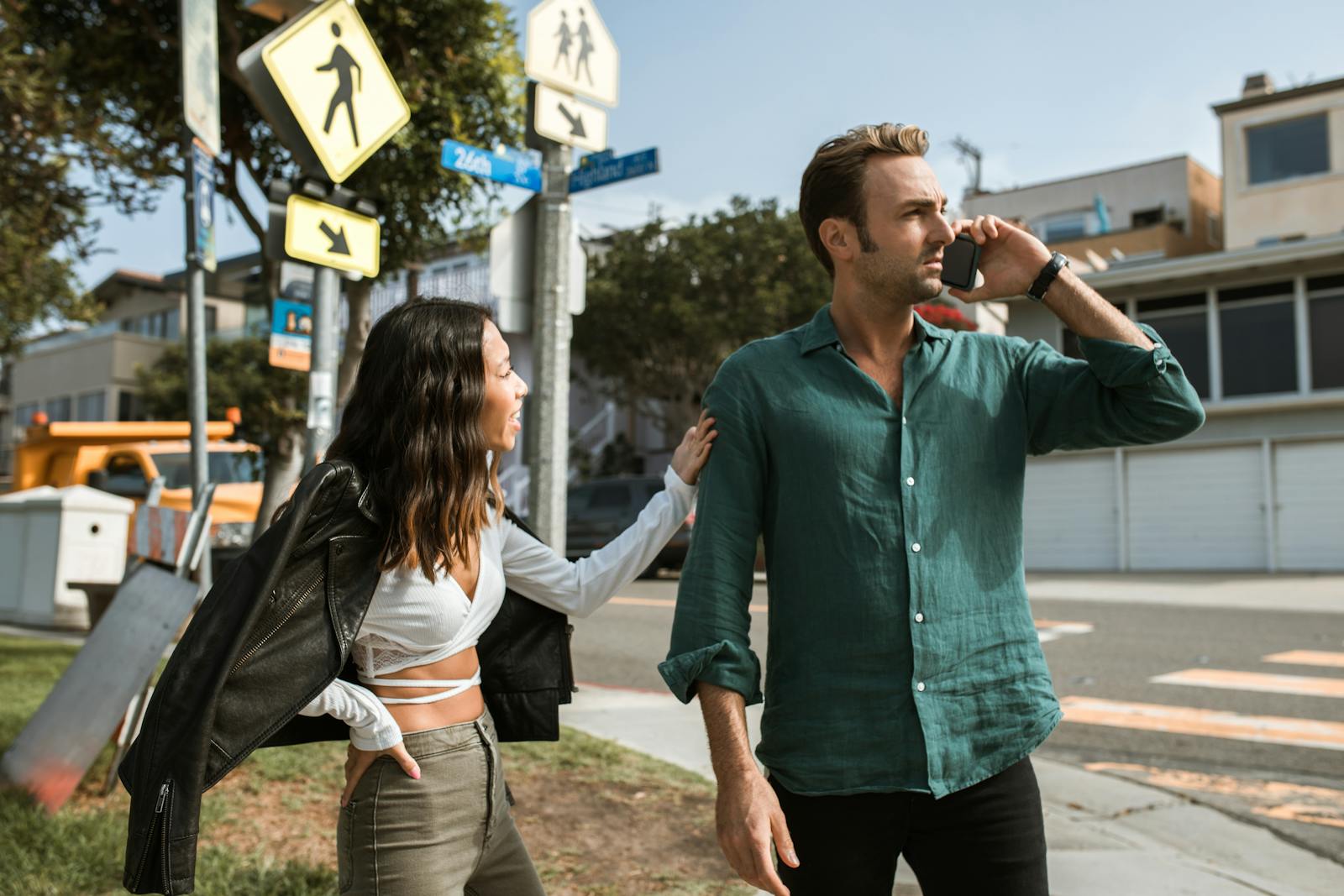 A couple has an intense discussion outdoors on a sunny street corner.