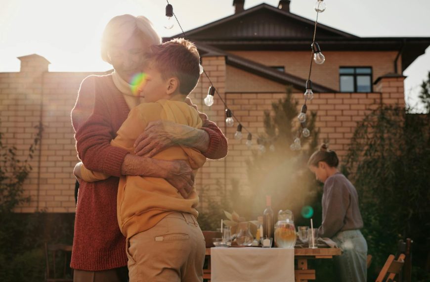 A grandmother hugging her grandson in a sunny backyard with an outdoor table setup.