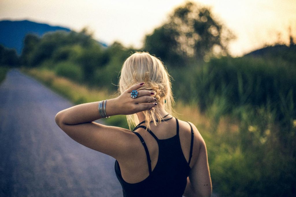 Blonde woman with bracelets walking on a path at twilight, showcasing fashion and nature.