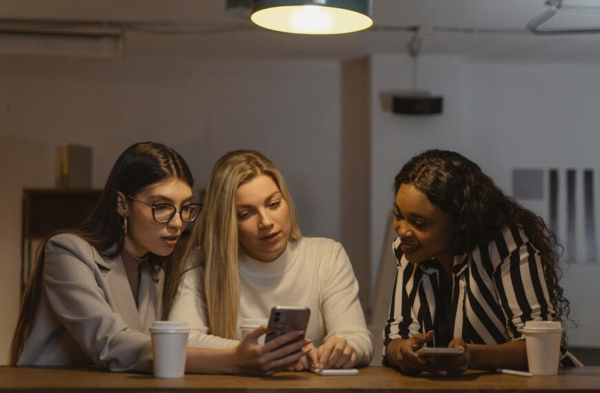 Three diverse women enjoying time together, interacting with smartphones at a table indoors.