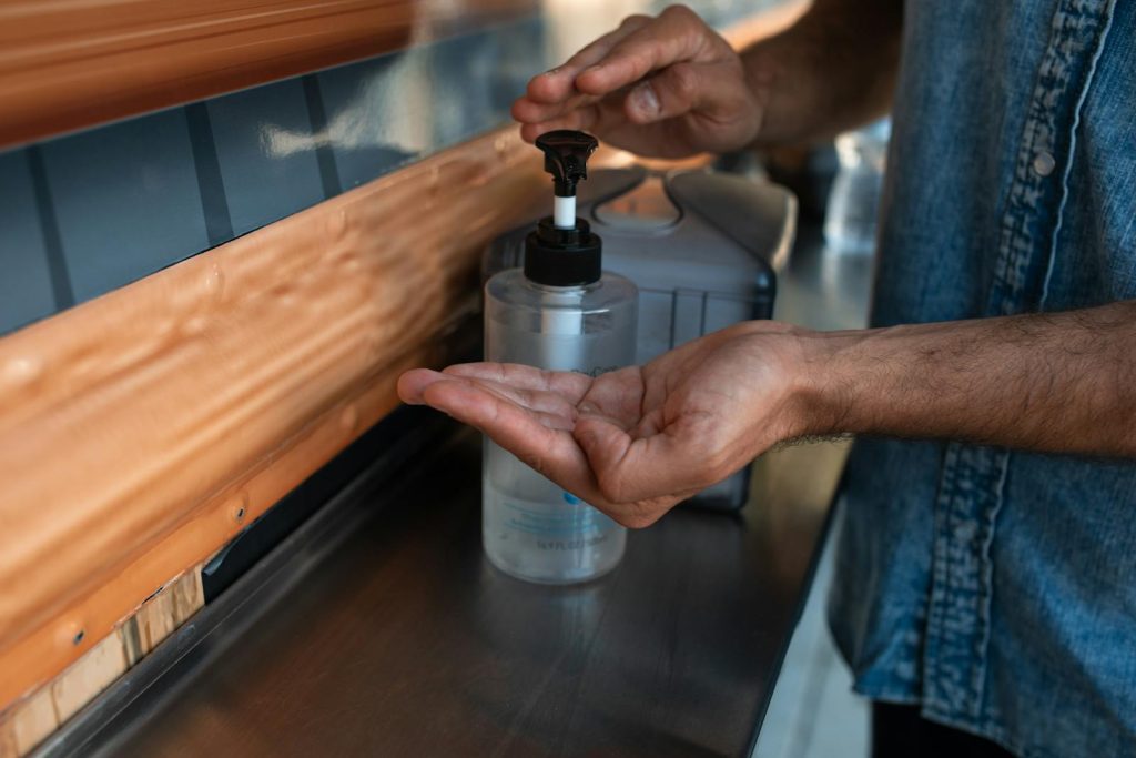 A person uses hand sanitizer from a dispenser to maintain hygiene in a public area.