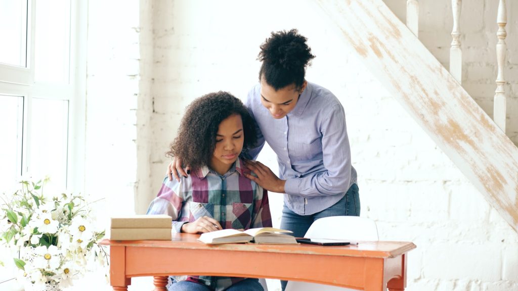 Mother helping daughter with homework at a desk.