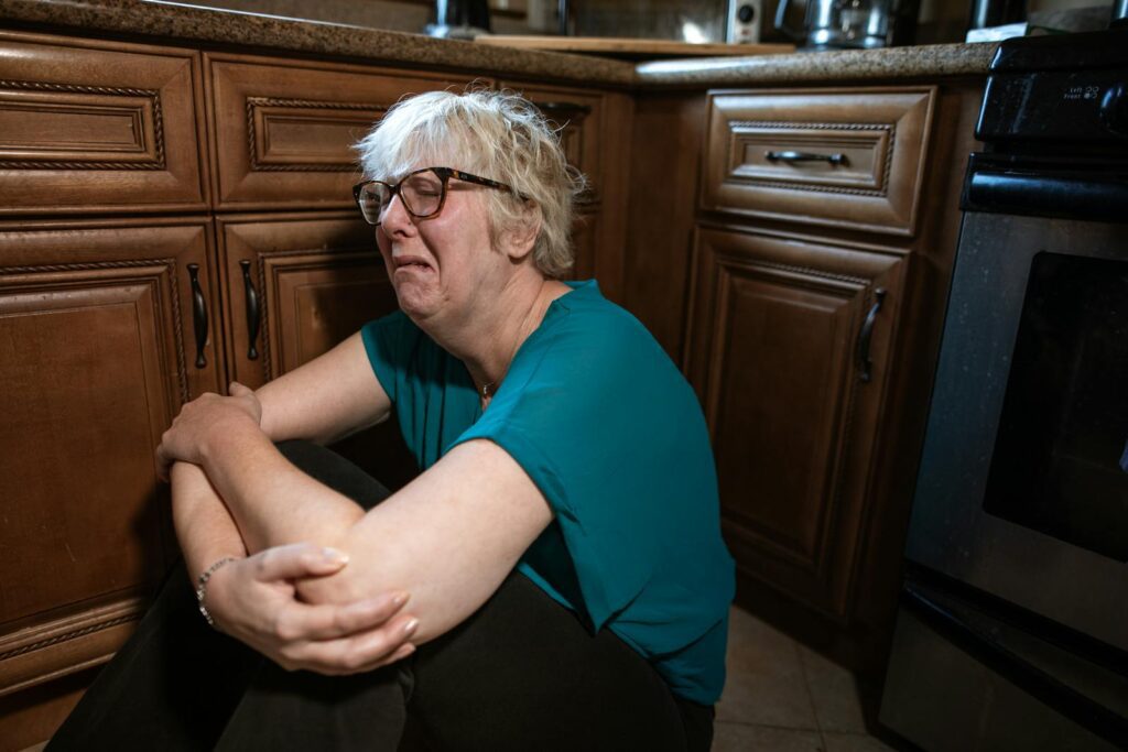 A distressed woman sitting on the kitchen floor, expressing deep emotion.