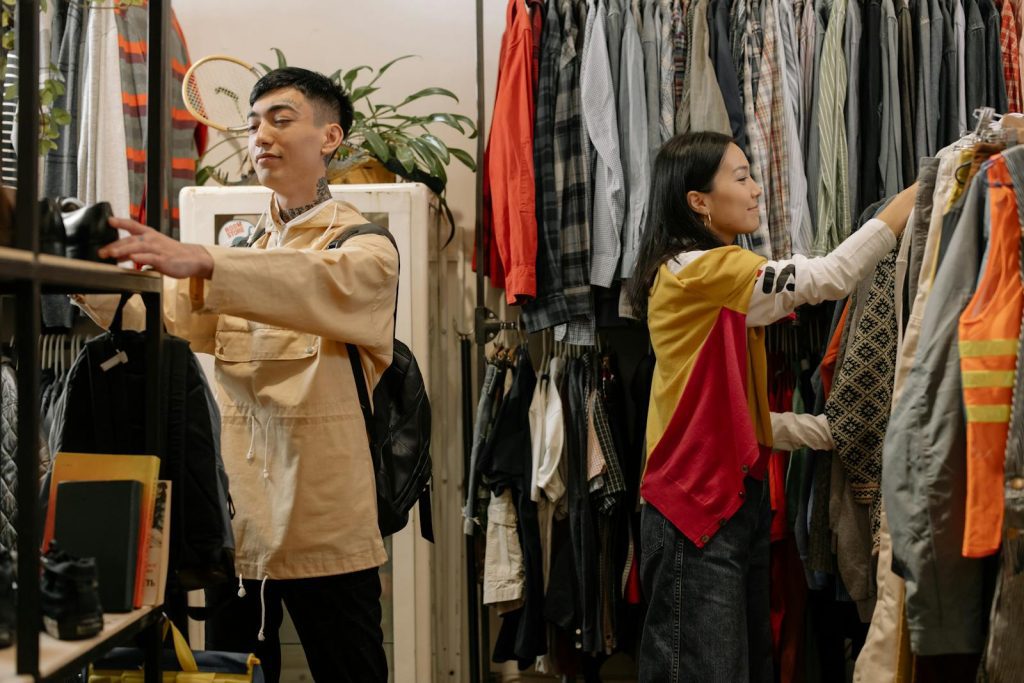 Two young adults selecting clothes in a crowded vintage thrift store.