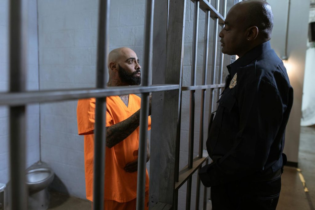 A guard converses with an inmate inside a prison cell, highlighting the justice system setting.