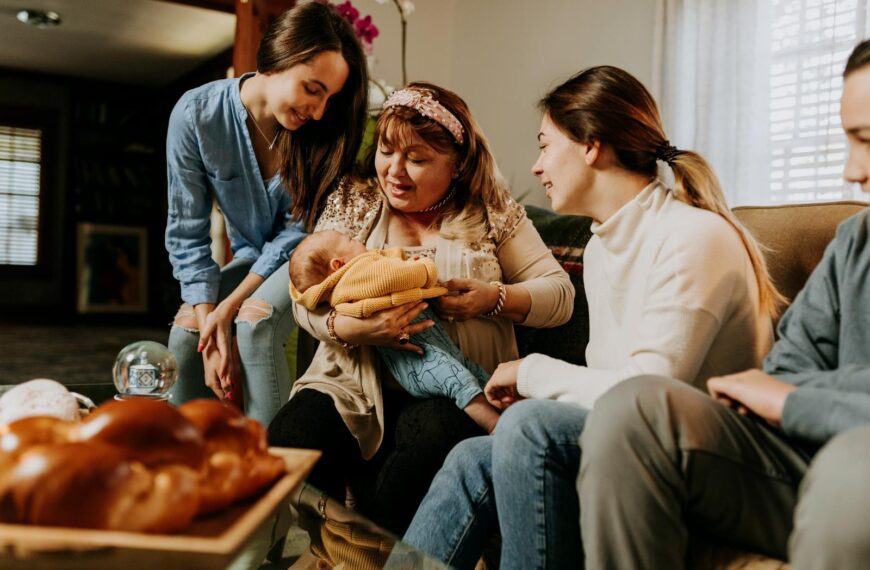 A touching family moment featuring a grandmother holding a baby surrounded by loved ones indoors.