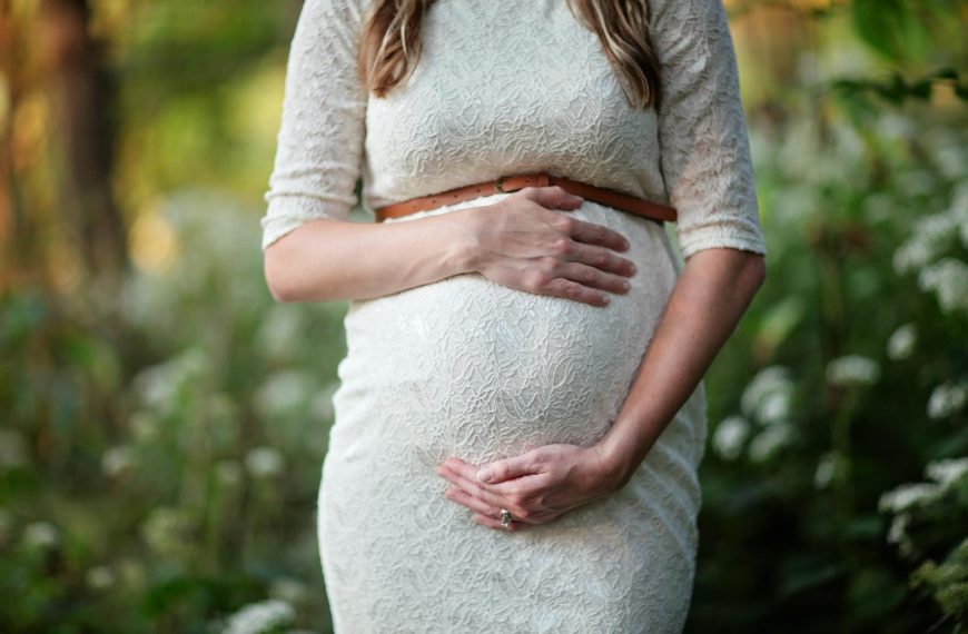 A pregnant woman in a lace dress gently cradling her belly in an outdoor setting.