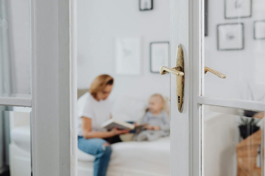 A mother lovingly reads to her daughter in a bright and cozy bedroom setting.