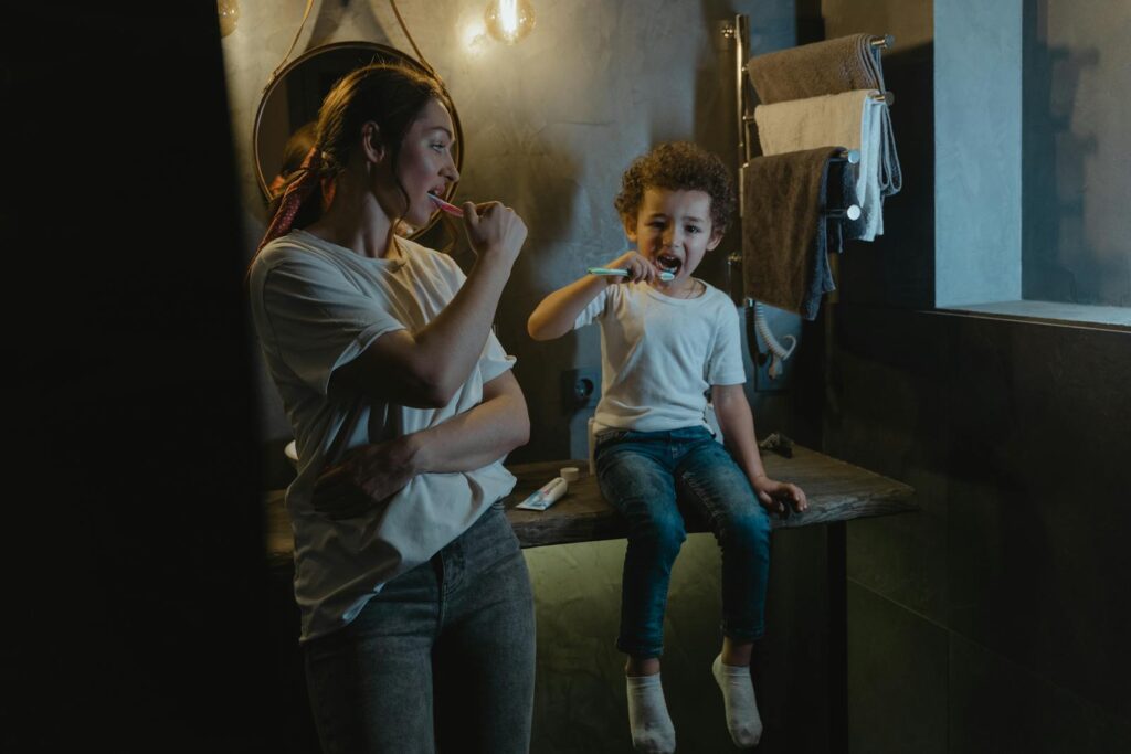 A mother and son brush their teeth together in a warmly lit bathroom, promoting good hygiene habits.
