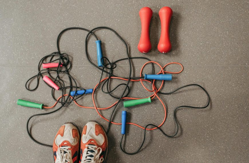 Top view of vibrant jump ropes and dumbbells on a gym floor, with sneakers visible.