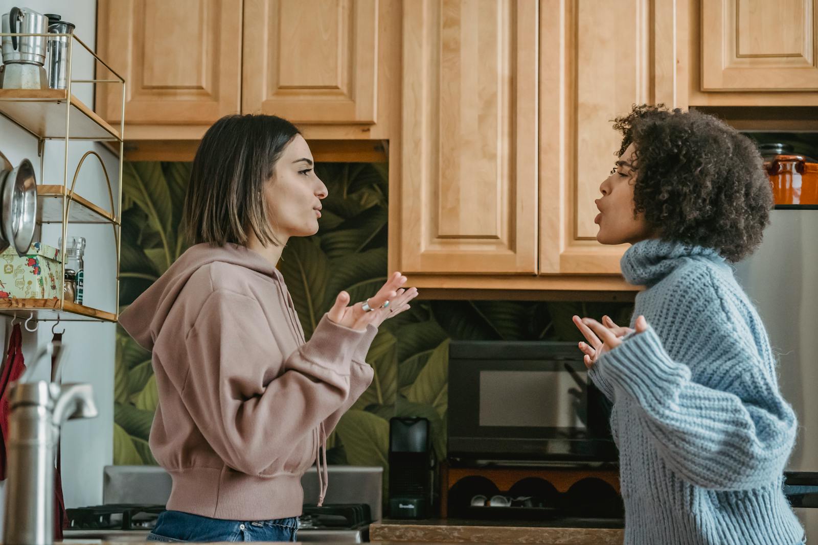 A heated discussion between two young women in a contemporary kitchen setting.