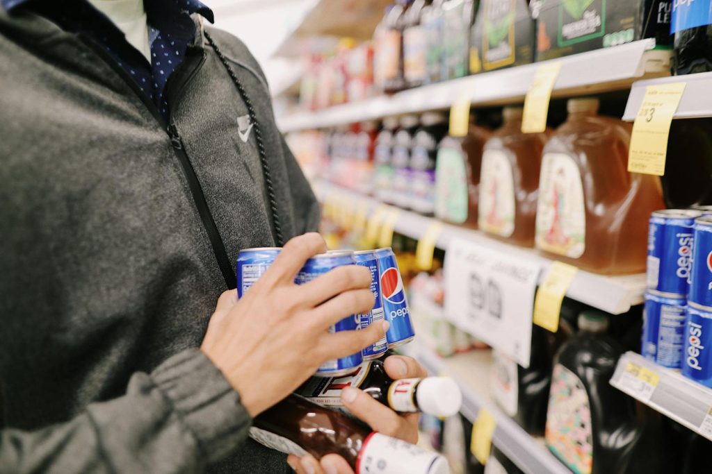 Close-up of an adult shopping for Pepsi and sauces in a grocery store aisle.