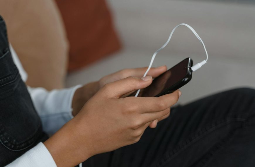 A person holds a smartphone with earbuds connected, capturing modern technology engagement.