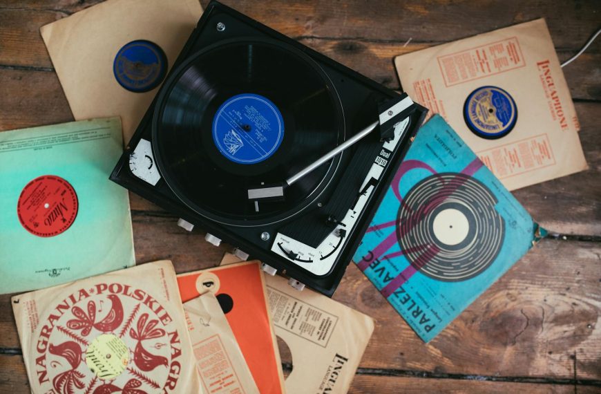 A collection of vintage vinyl records surrounding a classic turntable on a wooden floor.