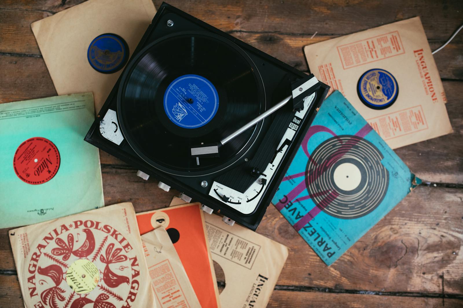 A collection of vintage vinyl records surrounding a classic turntable on a wooden floor.