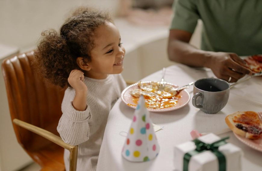 Smiling child with curly hair enjoying breakfast with family, celebrating indoors.