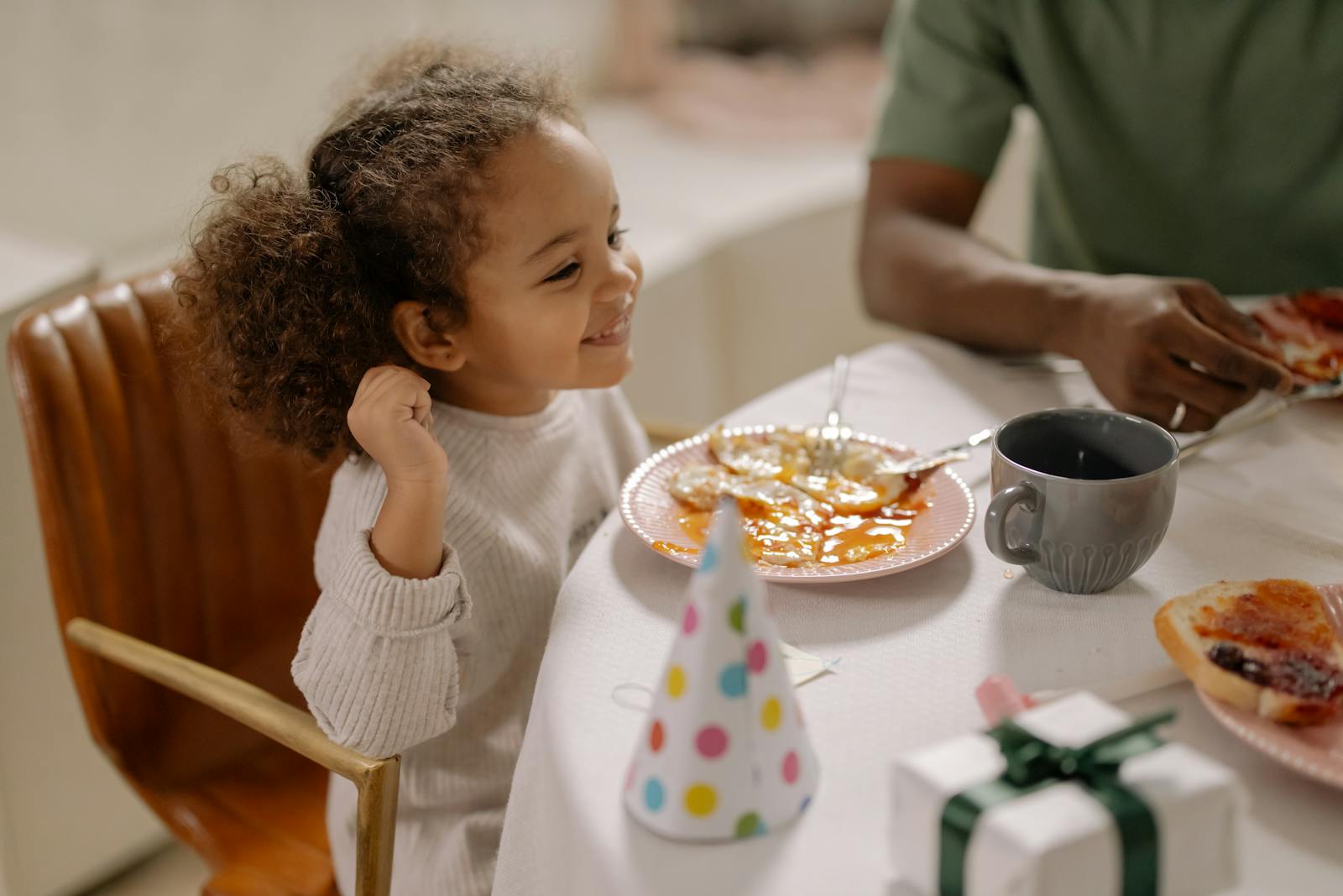 Smiling child with curly hair enjoying breakfast with family, celebrating indoors.
