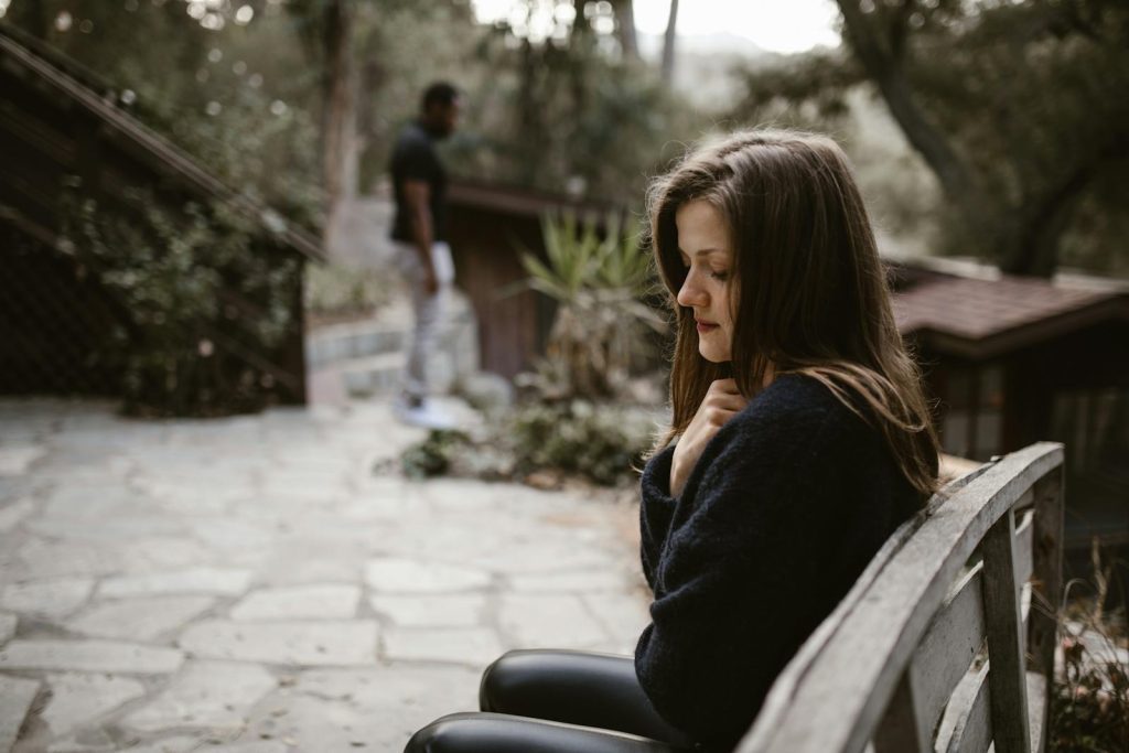 A woman sitting alone on a bench with a distant person, evoking a contemplative mood.