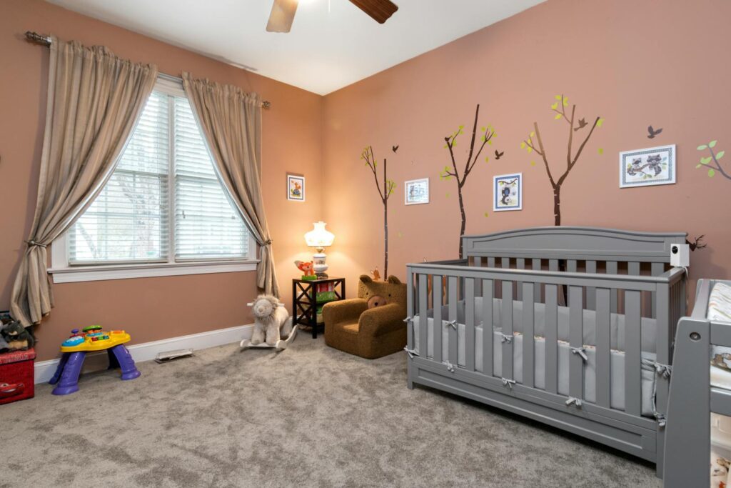 A cozy nursery featuring a grey crib, toys, and tree wall art with soft lighting.