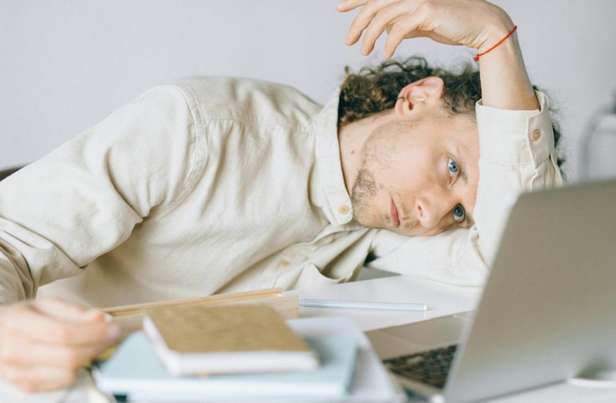 A tired Caucasian man at a desk, showing signs of exhaustion and stress, exemplifying workplace burnout.
