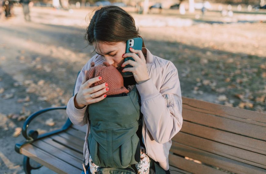 A mother affectionately kisses her baby while talking on the phone in a park setting.