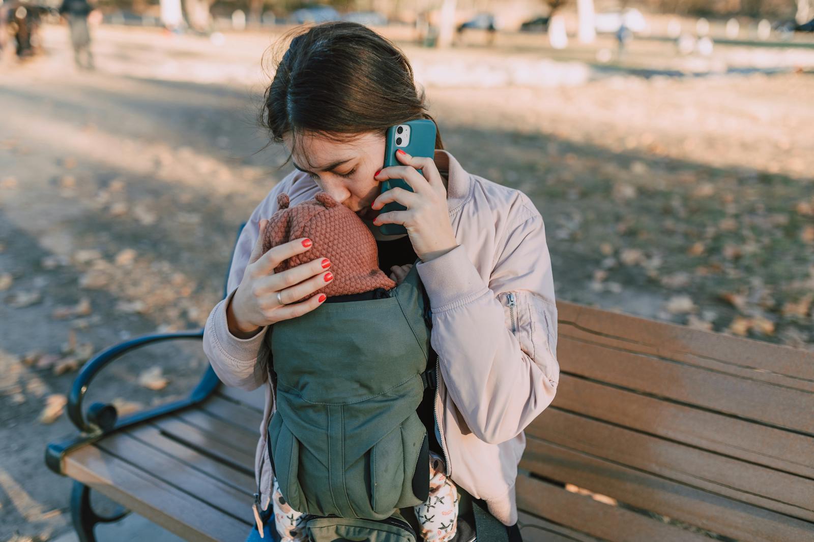 A mother affectionately kisses her baby while talking on the phone in a park setting.