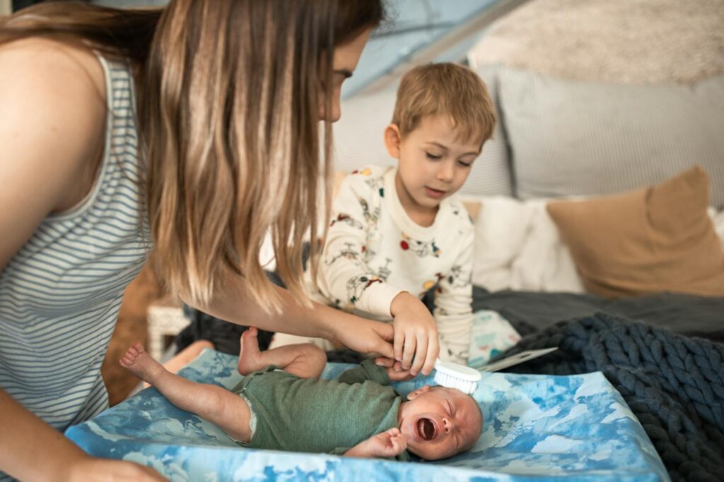 A caring mother and her children sharing a bonding moment while brushing the newborn's hair indoors.