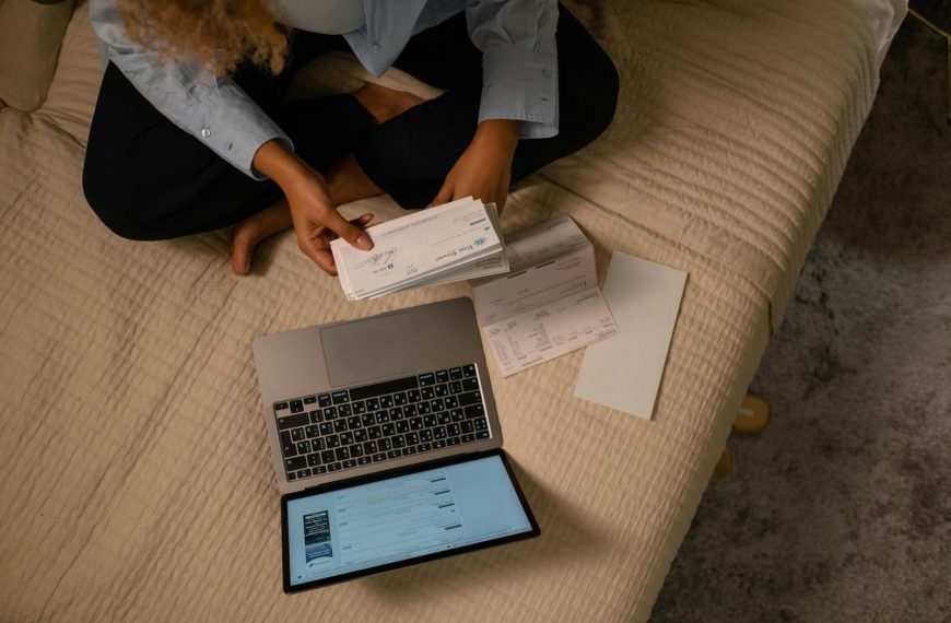 Overhead view of woman organizing finances on bed with laptop and checks.