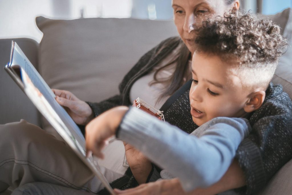 A grandmother and her young grandson share a cozy moment reading a book together on the couch.