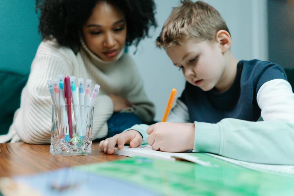 A young child writes while being supported by a teacher, focusing on learning.