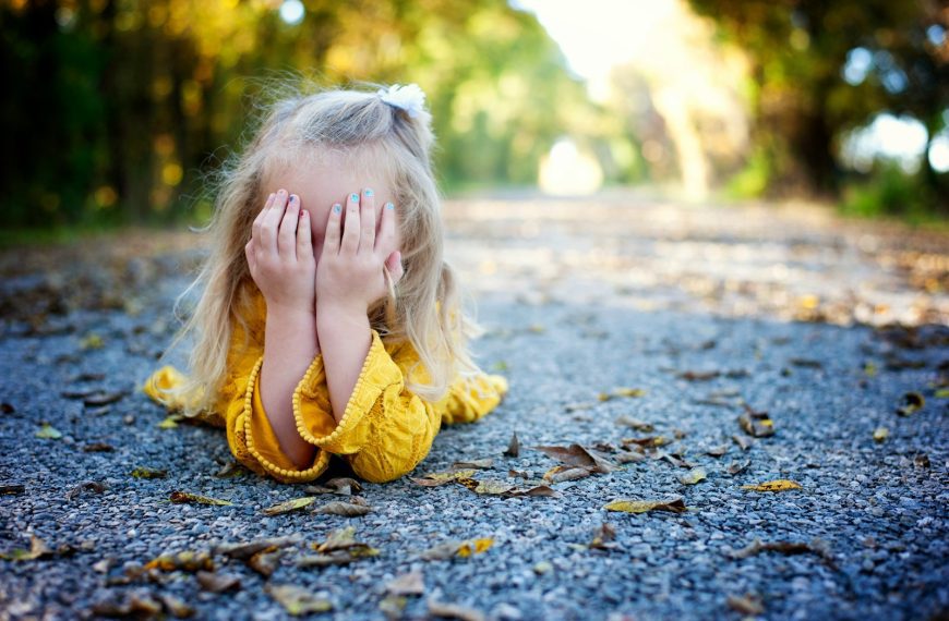 girl in yellow dress sitting on ground with dried leaves during daytime